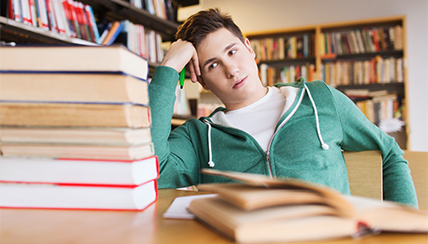 Boy looking at a stack of books with his had on his head