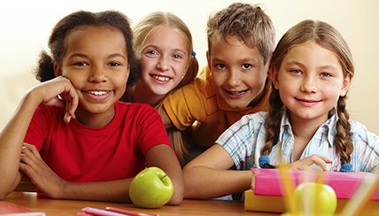 Children smiling with apples on table
