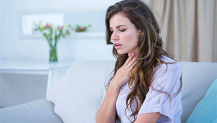 Woman rubbing her throat indoors