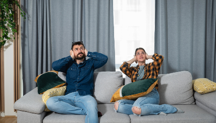 A couple sitting on the couch covering their ears